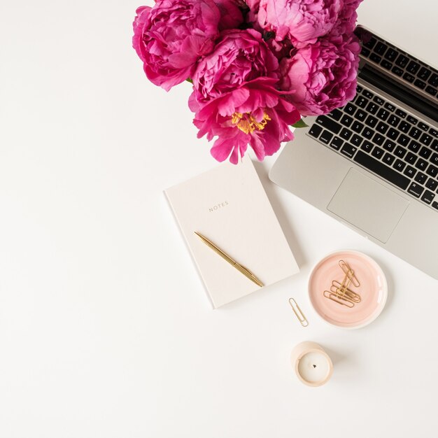 Laptop, beautiful pink peony tulip flowers bouquet and notebook on white table. Flat lay, top view