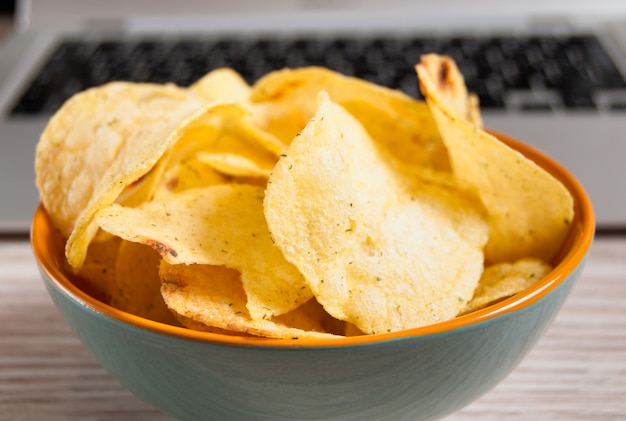 Laptop and bowl of chips on wood table. Bad habits concept