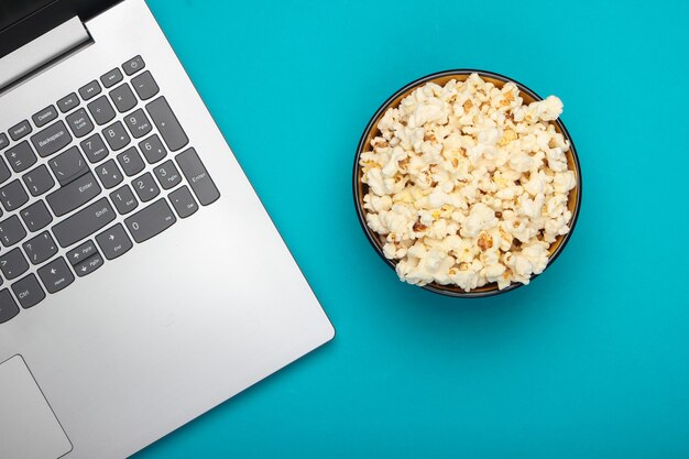 Laptop, bowl of popcorn on blue