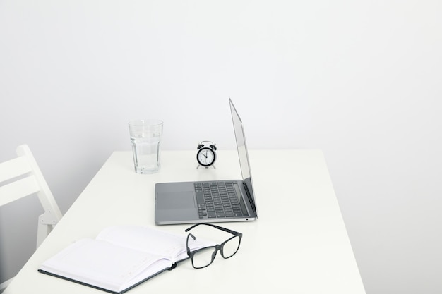 Laptop bril Kladblok glas en wekker op tafel op witte achtergrond ruimte voor tekst