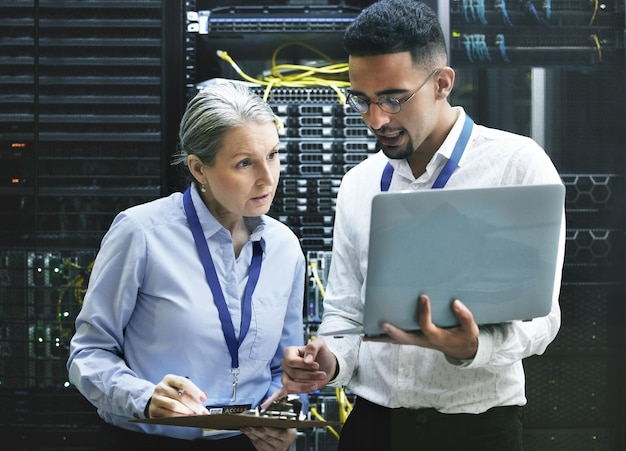 Foto appunti e tecnici del laptop in una sala server per l'installazione della tecnologia o la sicurezza informatica aggiornamento del sistema software digitale e senior manager che lavora al database di codifica con un programmatore maschio