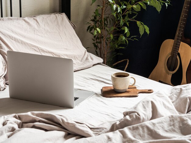 Laptop and coffee on the bed and a guitar next to the bed in the bedroom