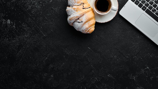 Laptop coffee and croissant Breakfast On a black stone background Top view Free space for your text