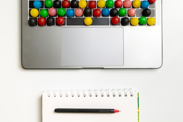 Computer portatile, caramelle colorate sulla tastiera e cartella di lavoro con cioccolato e caffè sul posto di lavoro.