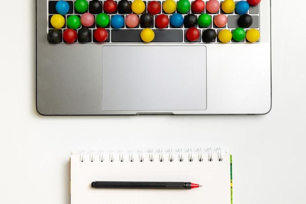 Laptop, colorful candy on keyboard and workbook with chocolate and coffee at workplace. 