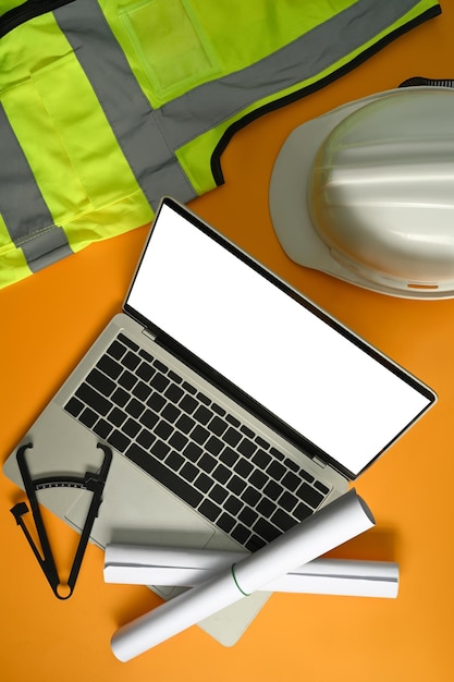 Foto laptop computer blauwdrukken veiligheidshelm koffiekopje en briefpapier op gele achtergrond