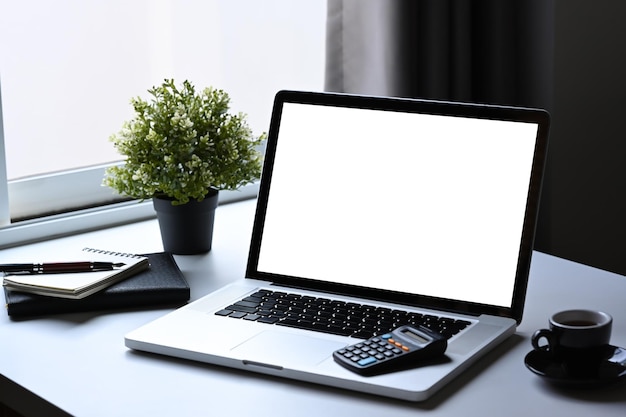 Laptop computer coffee cup notebook and calculator on white\
table empty display for graphic display montage