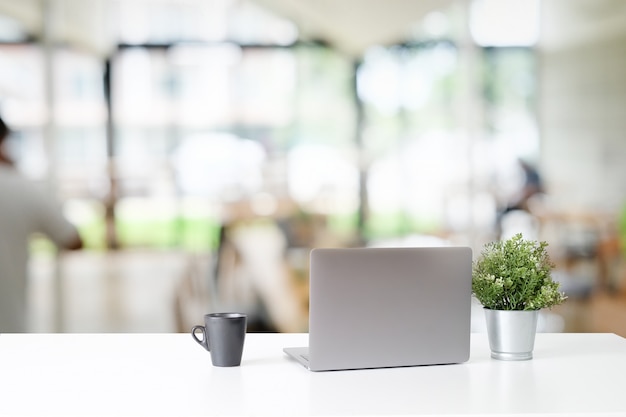 사무실에서 흰색 테이블에 노트북 컴퓨터와 커피 컵.