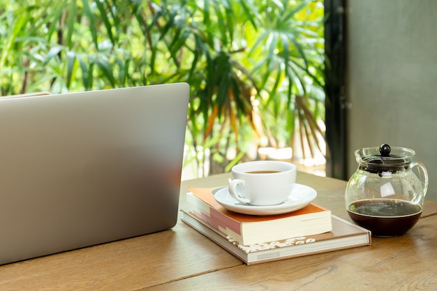 ラップトップコンピューターとカフェの木製のテーブルの上の本とコーヒーのカップ。