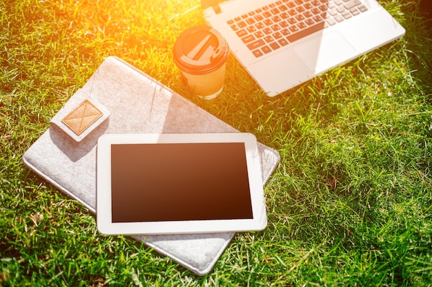 야외 공원에 커피 컵 가방과 태블릿이 있는 푸른 잔디에 있는 노트북 컴퓨터