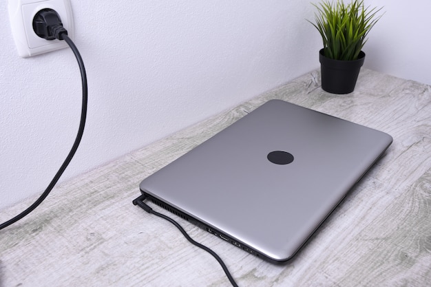 Laptop, computer is charging from a 220-volt outlet on a desk near the wall. Energy, accumulation.