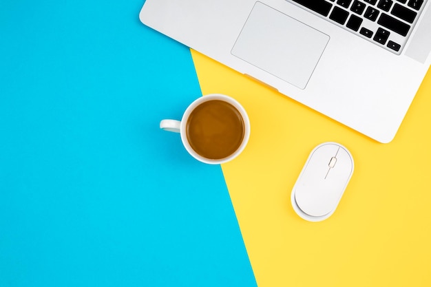 Laptop computer mouse and cup of coffee on a yellow and blue background