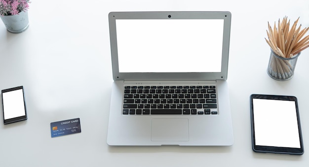 노트북 컴퓨터 또는 노트북 태블릿과 스마트폰 빈 흰색 화면은 집이나 사무실의 창가에 있는 책상 위에 놓여 있습니다.
