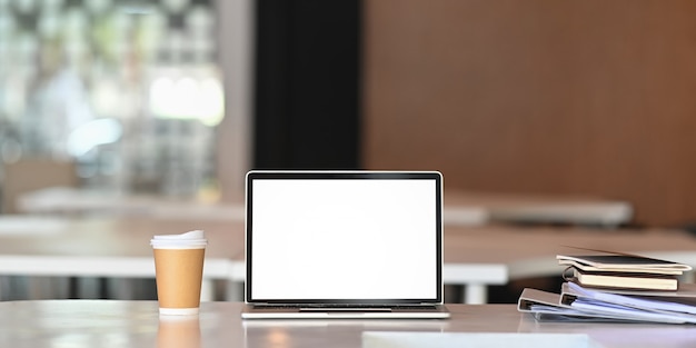 laptop computer, paper coffee cup, document file on business table with empty screen.