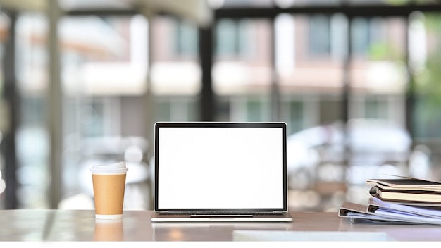 Laptop computer, paper cup and books on white desk.