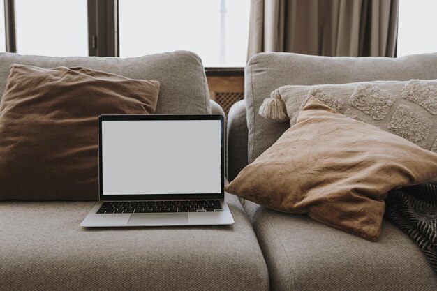 枕付きの快適なソファに空白のコピー スペース画面を備えたラップトップ コンピューター美的な家のリビング ルームのインテリア オンライン ショッピング オンライン ストア ソーシャル メディア ブログ ブランディング モックアップ テンプレート