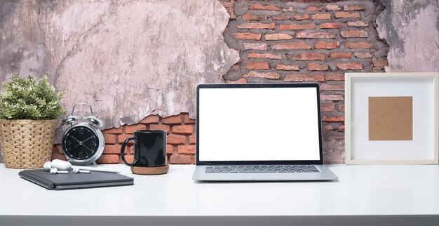 空白の画面のコーヒーカップの額縁と白いテーブルの上の鉢植えの植物とラップトップコンピュータースタイリッシュな職場