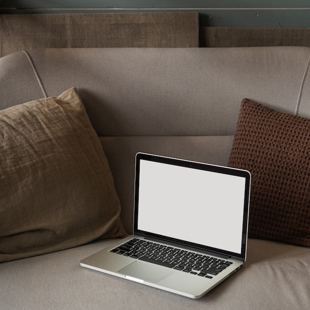 Photo laptop computer with blank screen on comfortable sofa with pillows