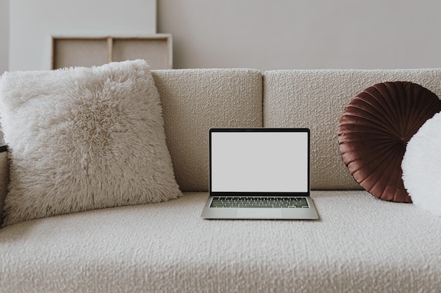 Photo laptop computer with blank screen on comfortable woolen sofa with pillows aesthetic template with mockup copy space online store blog social media website branding online shopping concept