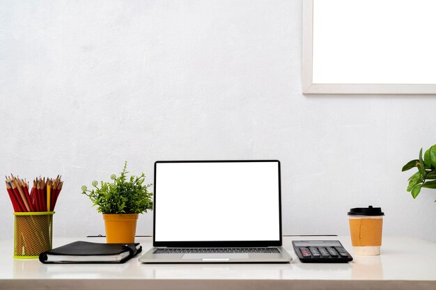 Laptop computer with blank screen home plant watering can unrecognizable picture in frame on dresser