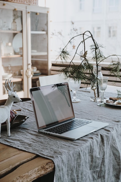 Laptop computer with blank screen on linen table cloth with fir spruce bouquet Christmas decorations Elegant home office working space interior design Work at home