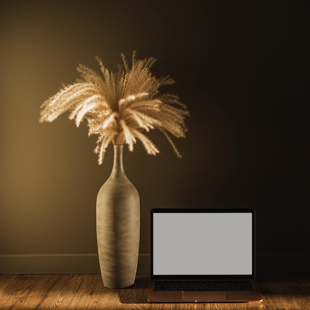 Computer portatile con bouquet di erba di pampa a schermo vuoto alla luce del sole ombre sul muro influencer estetico modello di interior design in stile boho con spazio di copia mockup