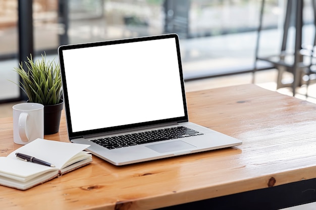 Laptop computer with blank screen on wooden table in office room.