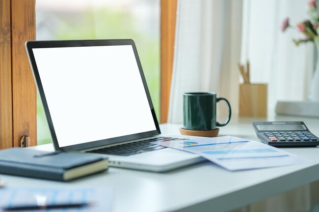 Laptop computer with empty screen stationery and potted plant on white table in bright office