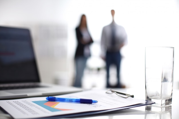 Laptop computer with folder on desk, two business people standing in the background