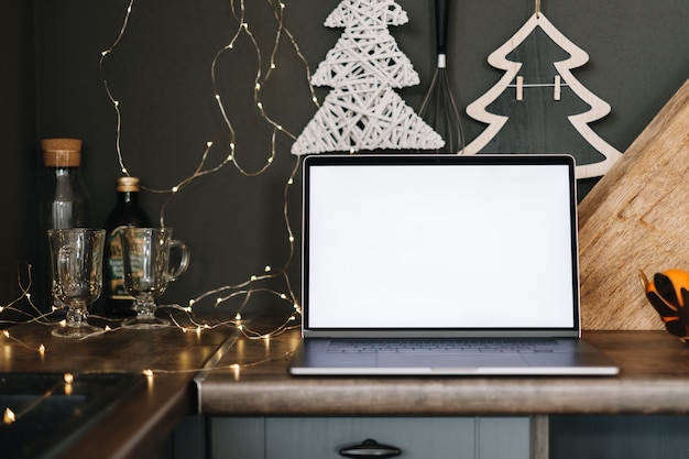 Laptop computer with white blank screen mock up, on the kitchen table with Christmas decoration.