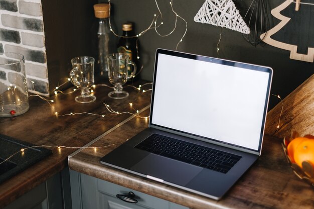 Photo laptop computer with white blank screen mock up, on the kitchen table with christmas decoration.