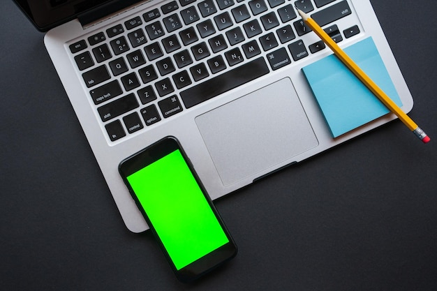 Laptop computer, yellow pencil, sticky notes and mobile telephone with green screen