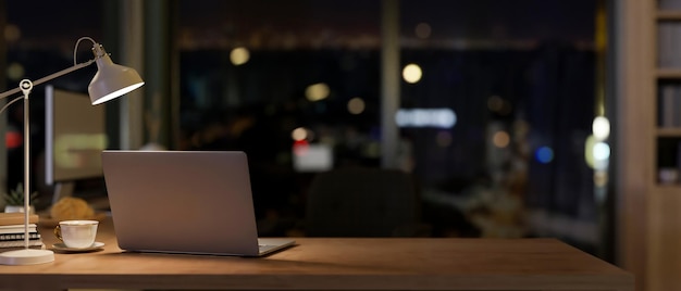 A laptop in a contemporary office room at night illuminated by dim lights from a table lamp