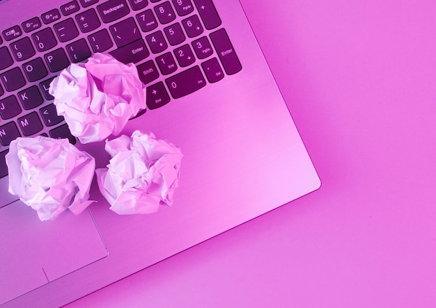 Laptop, crumpled paper balls close up. Holographic pink light