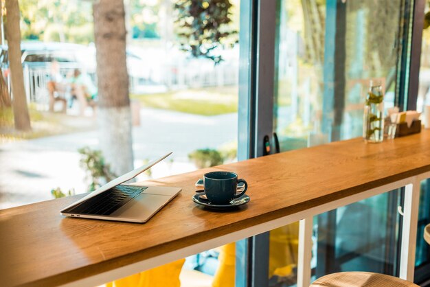 Laptop and cup of coffee on wooden cafe counter