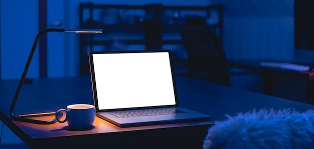 Laptop and cup on a table in a dark room with a blank screen at night