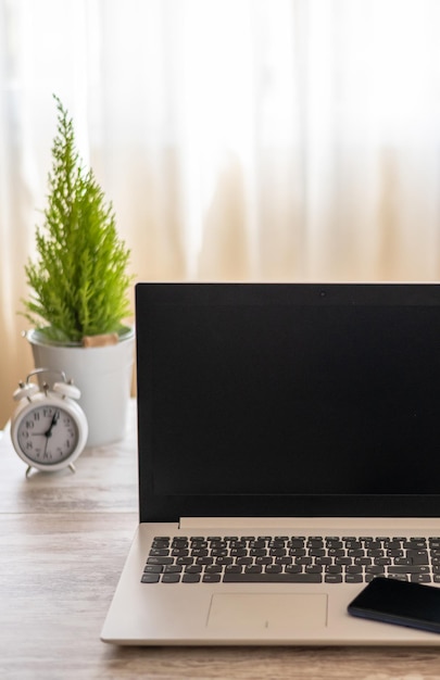 A laptop on a desk with a clock and a plant in the background