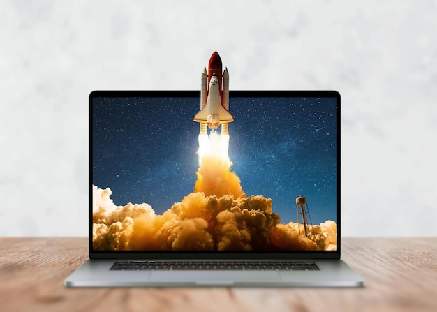 Foto il laptop sul desktop e il razzo dello space shuttle decollano con successo oltre le cornici del display avvio e successo idea creativa sviluppo marketing e concept applicativo