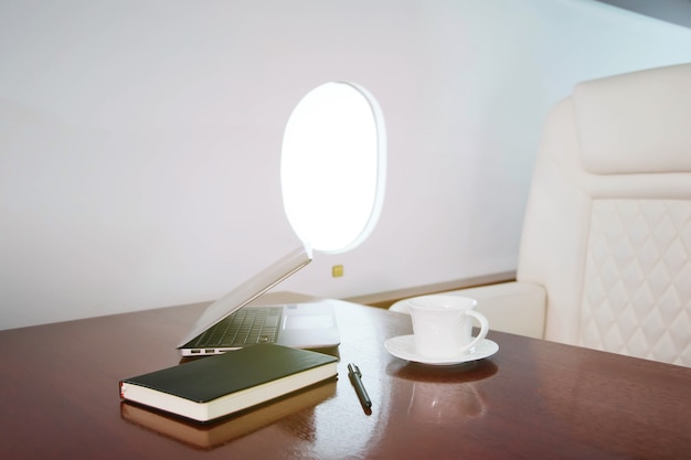 Laptop, diary and cup of coffee on table of luxury interior in private jet