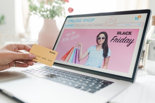 Дисплей ноутбука с заставкой черная пятница и женская рука с кредитной картой над клавиатурой, собирающаяся сделать заказ в интернет-магазине