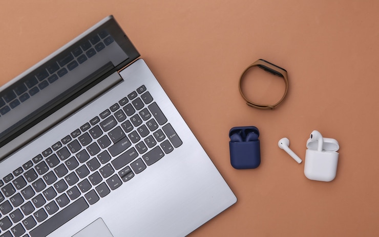 Foto laptop en draadloze koptelefoon met oplader en slimme armband op bruine achtergrond. bovenaanzicht