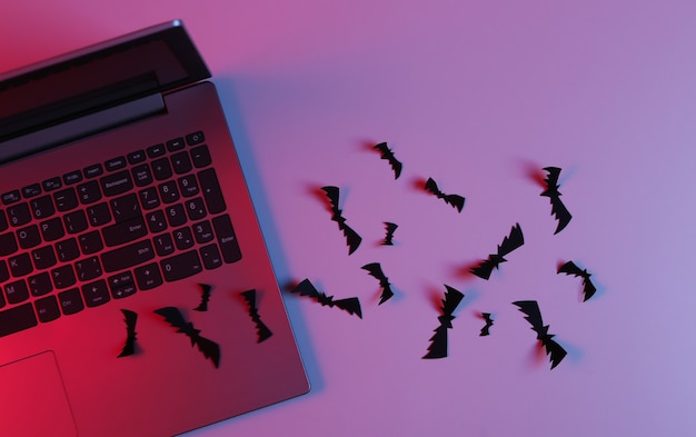 Laptop en Flying papier gesneden vleermuizen in neon blauw roze licht. Halloween-thema