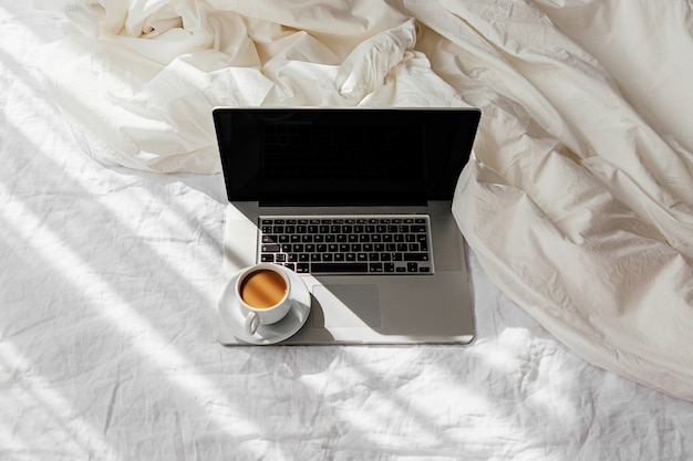 Laptop en kopje koffie op wit bed met een deken. Werk thuis concept. Ochtend licht. Lifestyle-concept