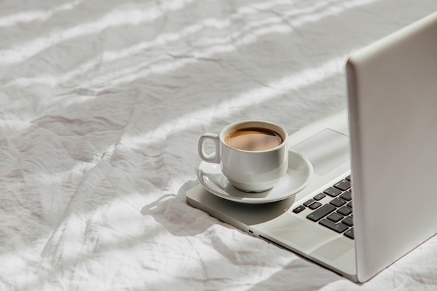 Laptop en kopje koffie op wit bed. Werk thuis concept. Ochtend licht