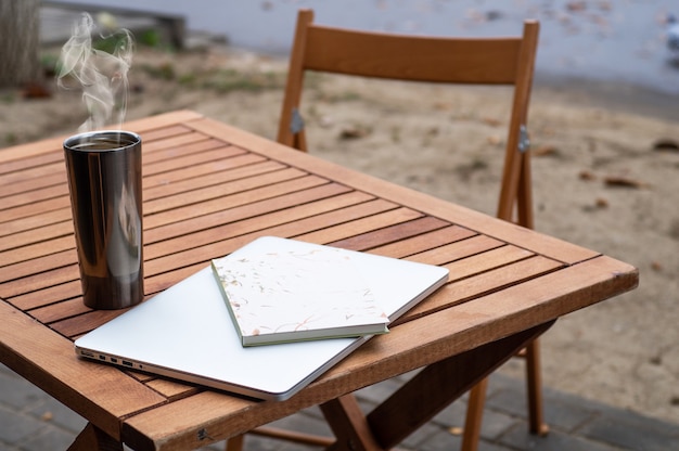 Laptop en thermo kopje koffie staat op een houten tafel in een café