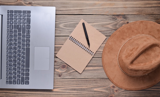 Laptop, felt hat, notebook and pen on a wooden table