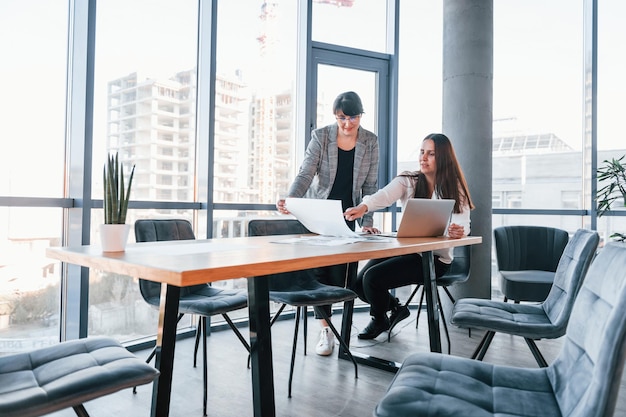 Laptop gebruiken Twee vrouwen in formele kleding zijn binnen in het moderne kantoor werken samen