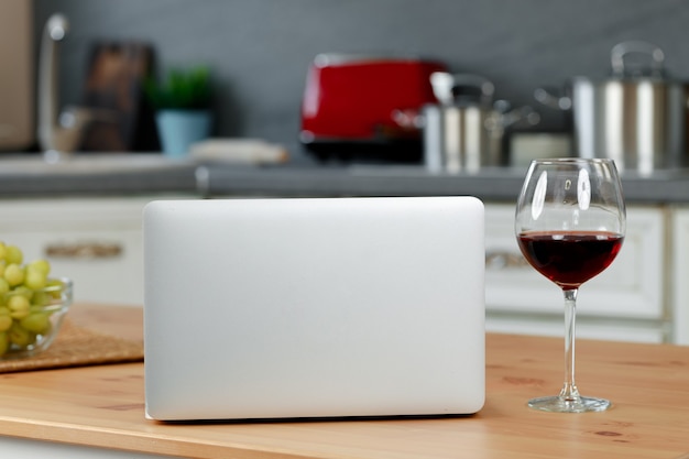 Laptop and glass of red wine on wooden kitchen table