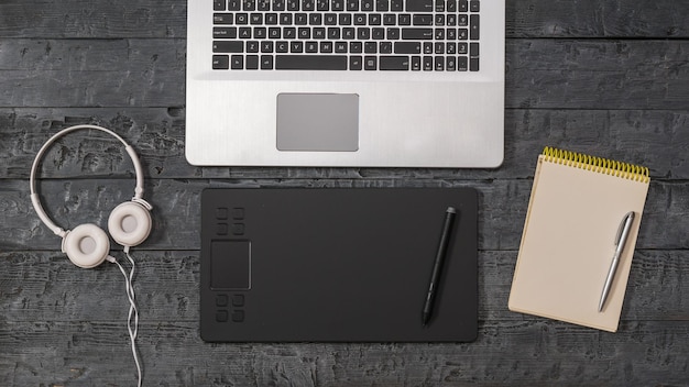 Laptop, graphic tablet, headphones and notebook on a wooden background. A device for working in image editors.