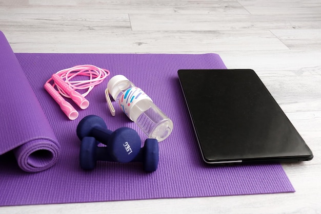 Laptop on gymnastic mat with sports equipment jump rope dumbbells and water bottle online sports